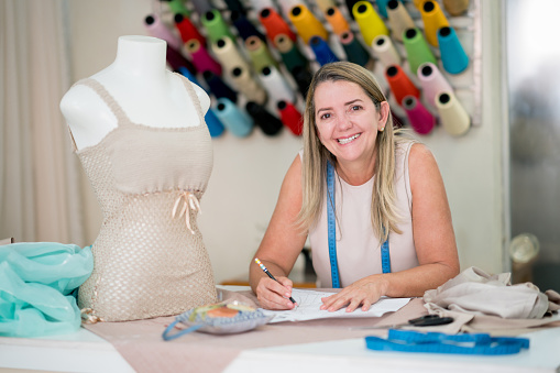 Portrait of a happy fashion designer drawing a dress pattern while working at an atelier and looking at the camera smiling