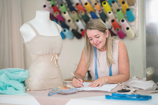 Portrait of a happy fashion designer drawing a dress pattern while working at an atelier making clothes