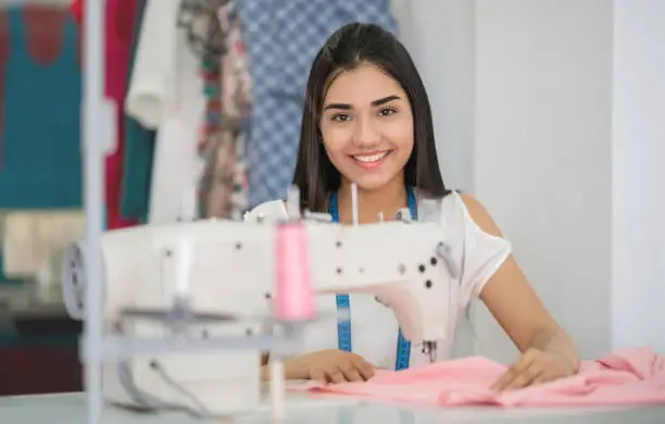 Happy seamstress sewing at an atelier and making a dress using a sewing machine - fashion industry concepts