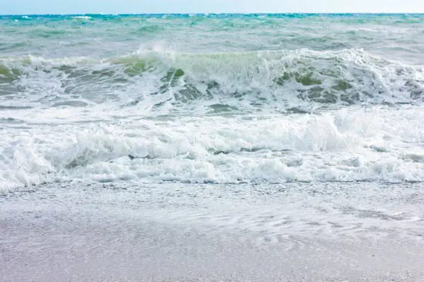 Photo of Stormy sea and blue sky, white sea foam on the yellow sandy beach.