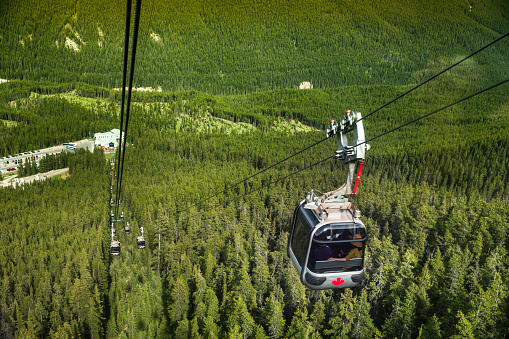 Tourist gondola cable car rises over the green forest to the top of Sulphur Mountain in Banff Alberta Canada