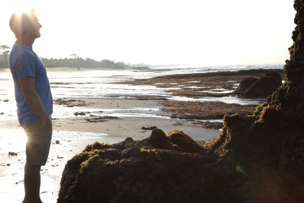 istock Man admires shrine on beach at sunrise 936924482