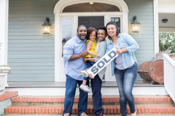 Family proud of their new home Attractive family smile proudly while holding a 'SOLD' sign in front of their new home. selling stock pictures, royalty-free photos & images