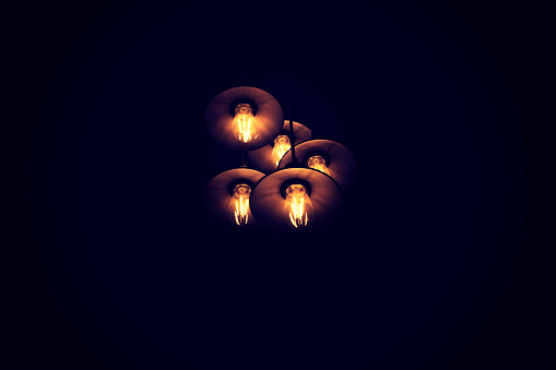 Series of lamps hanging from the ceiling in a dark room. Pitch black room around the lamps.m
