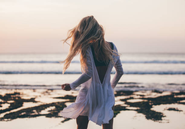 Beautiful blonde girl with long hair in short white dress dancing at sunset Beautiful blonde girl with long hair in short white dress dancing at sunset on the beach in Bali, Indonesia blonde model in dress stock pictures, royalty-free photos & images
