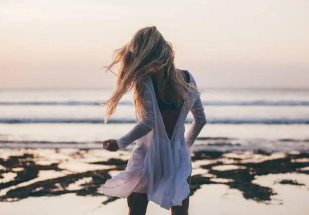 Photo of Beautiful blonde girl with long hair in short white dress dancing at sunset