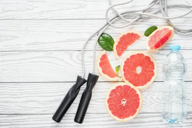 Jumping-rope, fresh grapefruits and bottle of water, on rustic white wooden table , top view, flat lay, fitness accessories. Concept of slimming, dieting and healthy nutrition.
