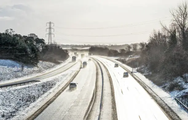 Traffic on the Edinburgh city bypass with bright light reflecting off the road surface, and the surrounding landscape covered in snow.