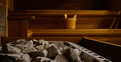 Wooden Bathhouse with a heating pot filled with stones, close up. Wooden sauna interior with equipment, coals, ladle, bucket.