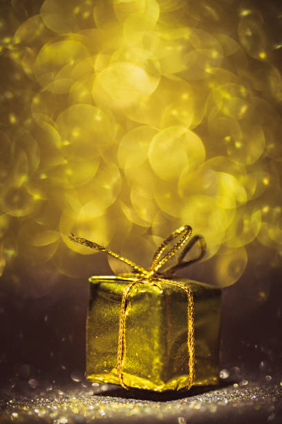 Golden metallic gift pack on gloden, glittery, bokeh background with huge copy space and shallow depth of field effect.