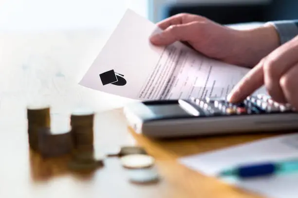 Photo of Man counting college savings fund, tuition fee or student loan with calculator. Education price and expenses concept. Money and papers on table.