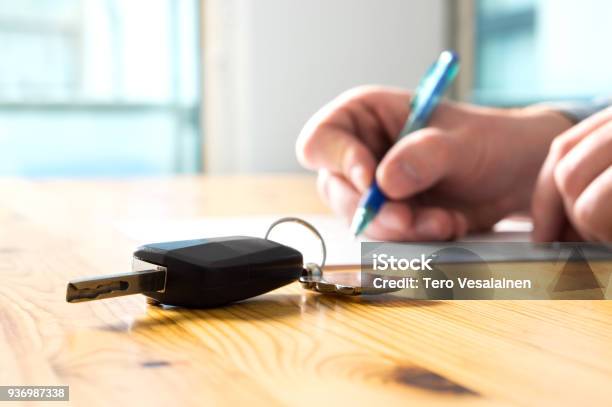 Man Signing Car Insurance Document Or Lease Paper Writing Signature On Contract Or Agreement Buying Or Selling New Or Used Vehicle Car Keys On Table Warranty Or Guarantee Stock Photo - Download Image Now