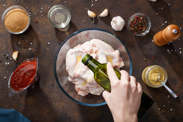 Hand pouring oil over raw chicken wings in glass bowl. stock photo