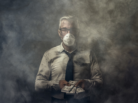 Greedy business executive wearing a mask and holding cash banknotes: pollution and corruption concept