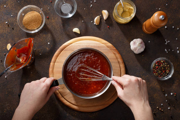 Hands mix the bbq sauce with the whisk in the saucepan. stock photo
