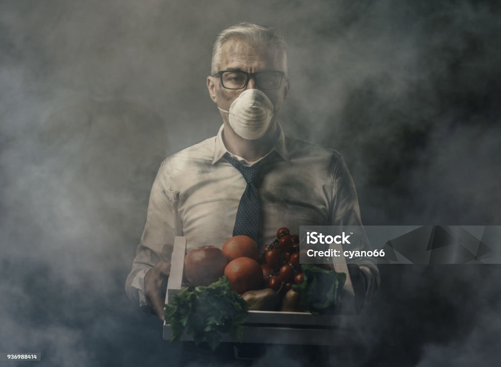 Food pollution and contamination Businessman with protective mask holding a crate with polluted poisonus vegetables, food pollution concept Food Stock Photo