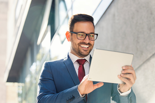 Smiling young businessman using tablet in front of the office