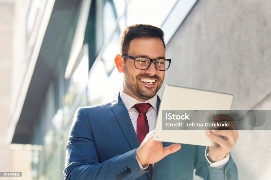 Businessman Smiling young businessman using tablet in front of the office Digital Tablet Stock Photo