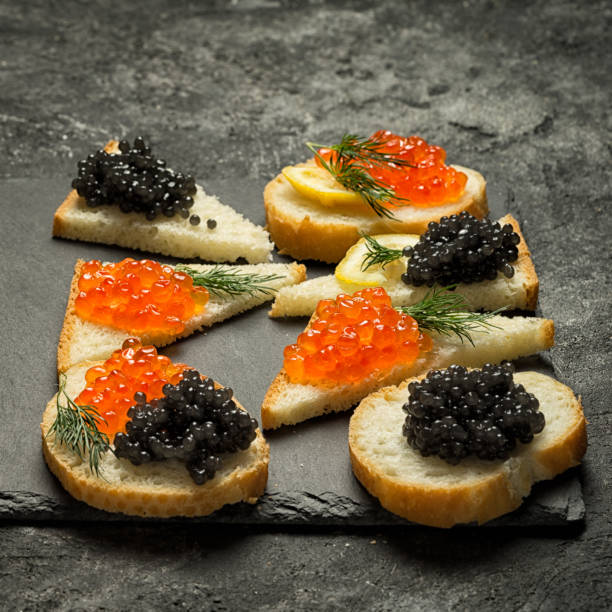istock Sandwiches with red and black fish caviar on a dark black background, square composition. 936995490