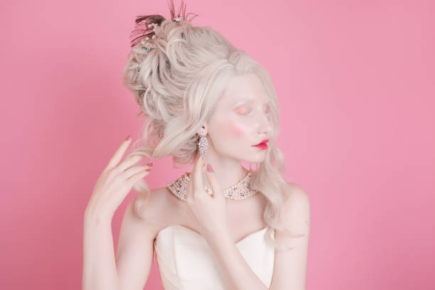 uma mulher loira com um estilo de cabelo de rococó luxuoso linda em um vestido branco sobre um fundo rosa. - princess hairstyle baroque style women - fotografias e filmes do acervo