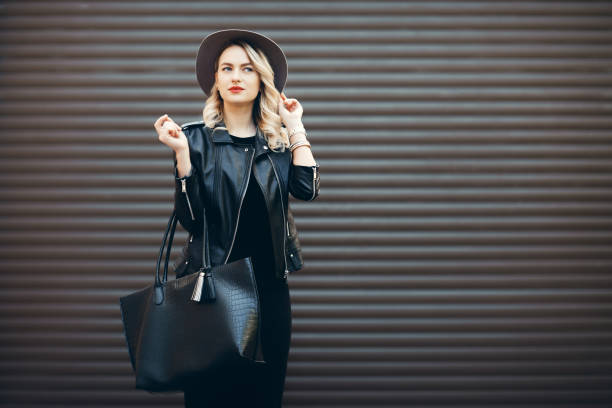 street portrait of glamour sensual young stylish lady wearing trendy fall outfit. blonde woman in black hat and leather jacket and bag. - casaco de couro imagens e fotografias de stock