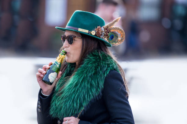 elegante vestido mujer racegoer disfrutando una bebida temprano de champagne, mezclándose con las muchedumbres grandes en cheltenham en su camino al mundo famoso cheltenham festival de caza. vestido con el verde de irlanda. - smartly fotografías e imágenes de stock