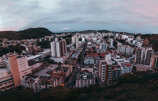 Wide-angle view from a high above of dark evening cityscape of a small Brazilian town Juiz de Fora in the Minas Gerais state: central street; many residential, office buildings, hills on the horizon