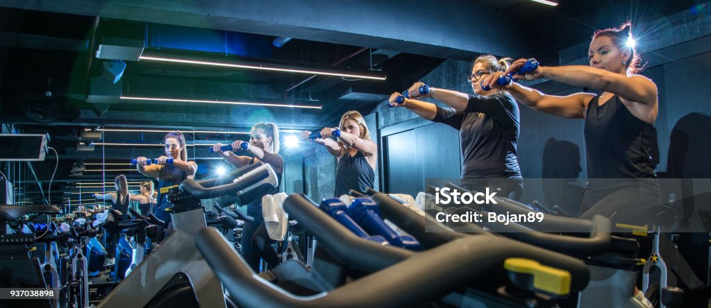 Panoramablick über sportliche Mädchen machen Übungen mit Gewichten während der Fahrt Fahrrad Fitness im Fitness-Studio - Lizenzfrei Trainingsraum - Freizeiteinrichtung Stock-Foto