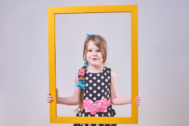 istock Beautiful little girl, with a funny expression on his face, holding a yellow frame 937057252