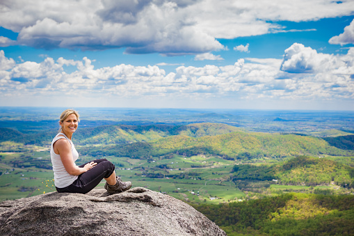 Beautiful mid 30s hiker woman sitting on a rock relaxing on the Old Rag Mountain trail in Shenandoah Valley National Park in Virginia