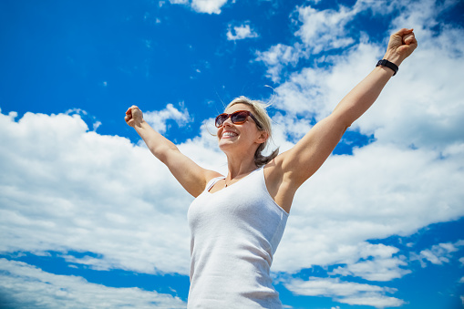 Beautiful mid 30s carefree woman with arms outstretched against a blue sky on a sunny day