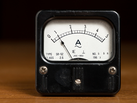 Closeup of an old black analog ampere meter on a wooden table