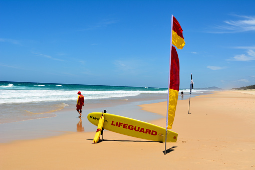 Noosa, Queensland, Australia - December 20, 2017. Surf lifesaver near red-yellow flag and rescue board at Sunshine Beach south of Noosa, QLD.