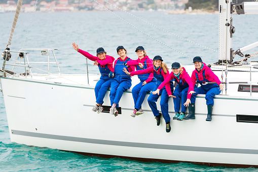 Group of Women Sitting on the Edge of a Sailing Ship Wearing Identical Clothes, Blue Working Pants and Pink Shirts