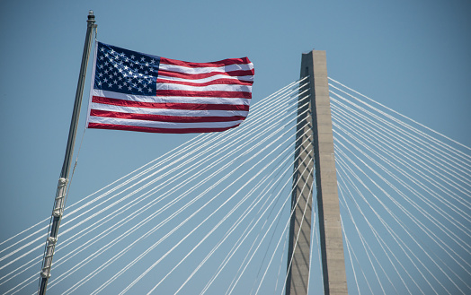 An American flag waves in the wind in front of the Cooper River Bridge in Charleston, SC.