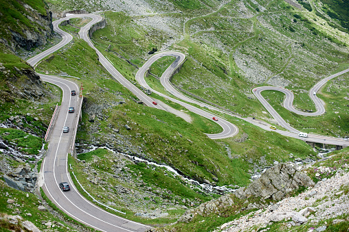 Cars driving popular among tourists beautiful winding Transfagarashan road in Romania. Green grassy path route rocky trees mountain hill slope highway attraction nature landscape view