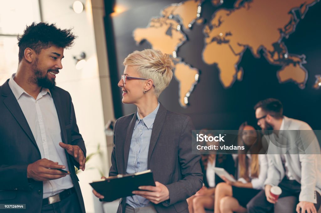 Business people working Businessman and businesswoman reviewing contract; business team working in the background. Focus on the man in the foreground Global Business Stock Photo