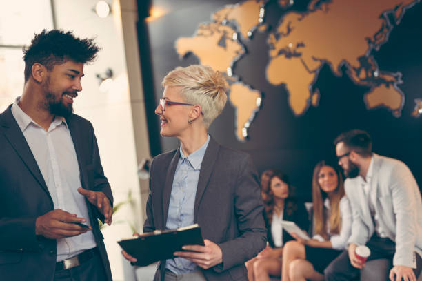 Business people working Businessman and businesswoman reviewing contract; business team working in the background. Focus on the man in the foreground global stock pictures, royalty-free photos & images