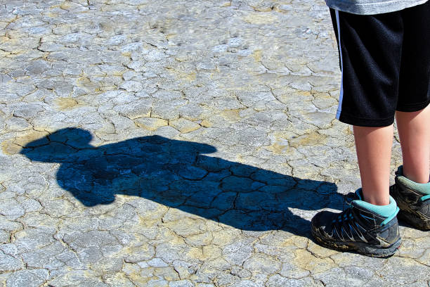 Shadow of a woung boy on dried mud.