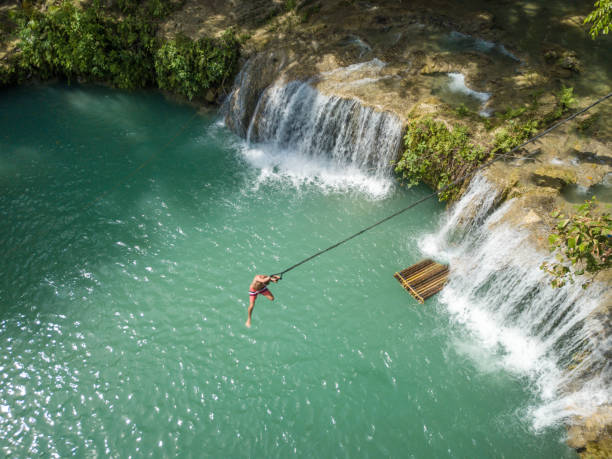 Drone point of view of man jumping into waterfall pool
