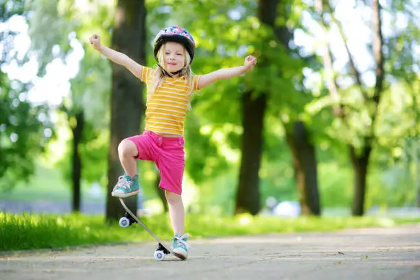 Photo of Pretty little girl learning to skateboard on beautiful summer day in a park