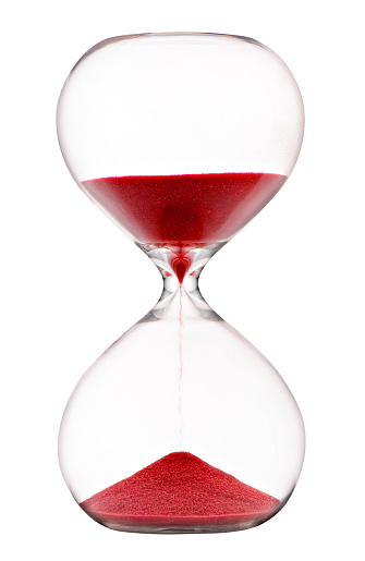 Red sand running through an hourglass with clear glass bulbs measuring passing time counting down to a deadline isolated on white