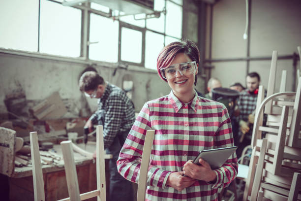 istock Young Smiling Carpenter in Front of Working Team in her Work Shop 937188072