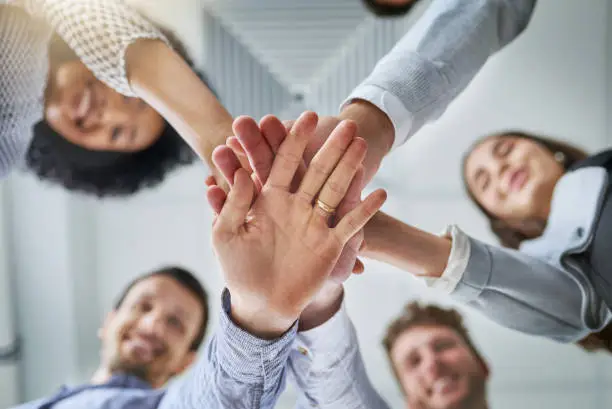 Low angle shot of a group of businesspeople joining their hands in a huddle in an office