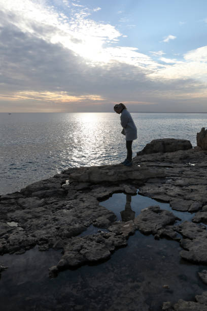istock Woman looks over rock edge by sea. 937217800