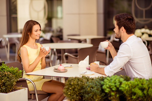 Yummy morning. Two cute lovers are sitting in light cafe on a sunny day and enjoy coffee with tasies, talking, smiling, looking at each other