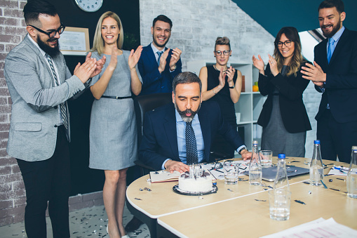 Group of people making surprise for their CEO with cake for retirement.