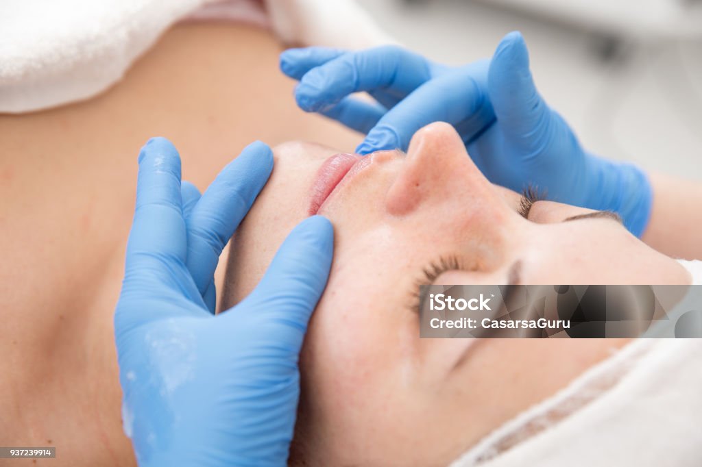 Adult Woman at Dermatology Skin Refreshing Treatment Dermatologist Applying Vaseline to Patient's Face After Microdermabrasion Treatment. Dermatology Stock Photo