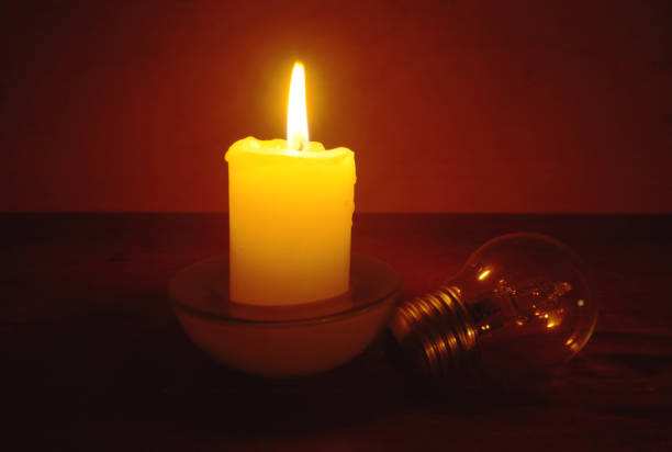 Burning candle and lamp on desktop in darkness. Troubles with electricy after storm.