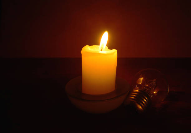Burning candle and lamp on desktop in darkness. Troubles with electricy after storm.